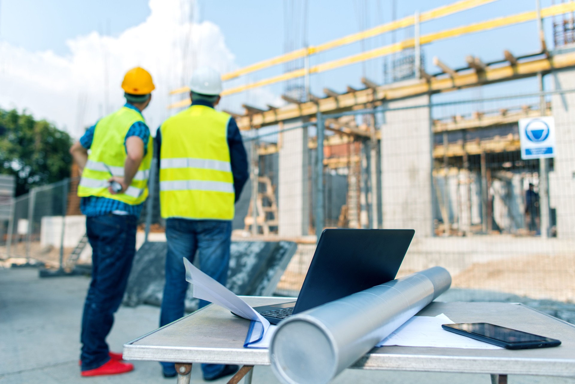 Construction workers behind blueprints and laptop on construction site